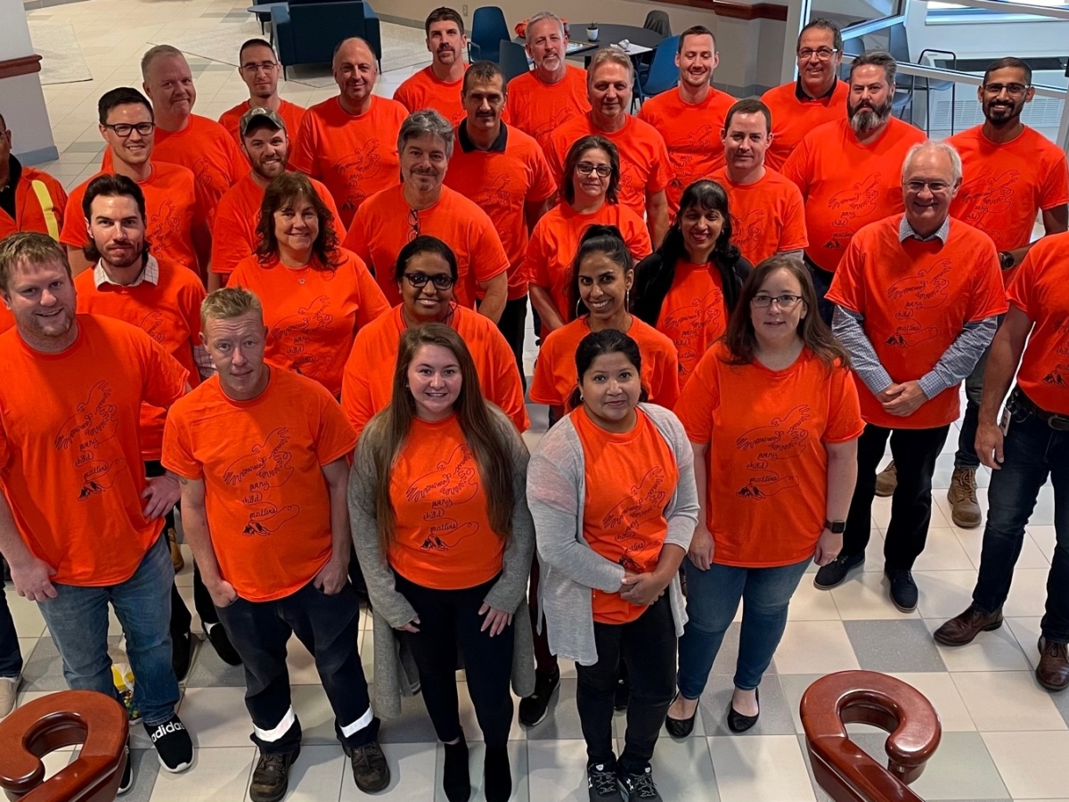 A group of staff stand together, wearing orange shirts, and smiling at the camera